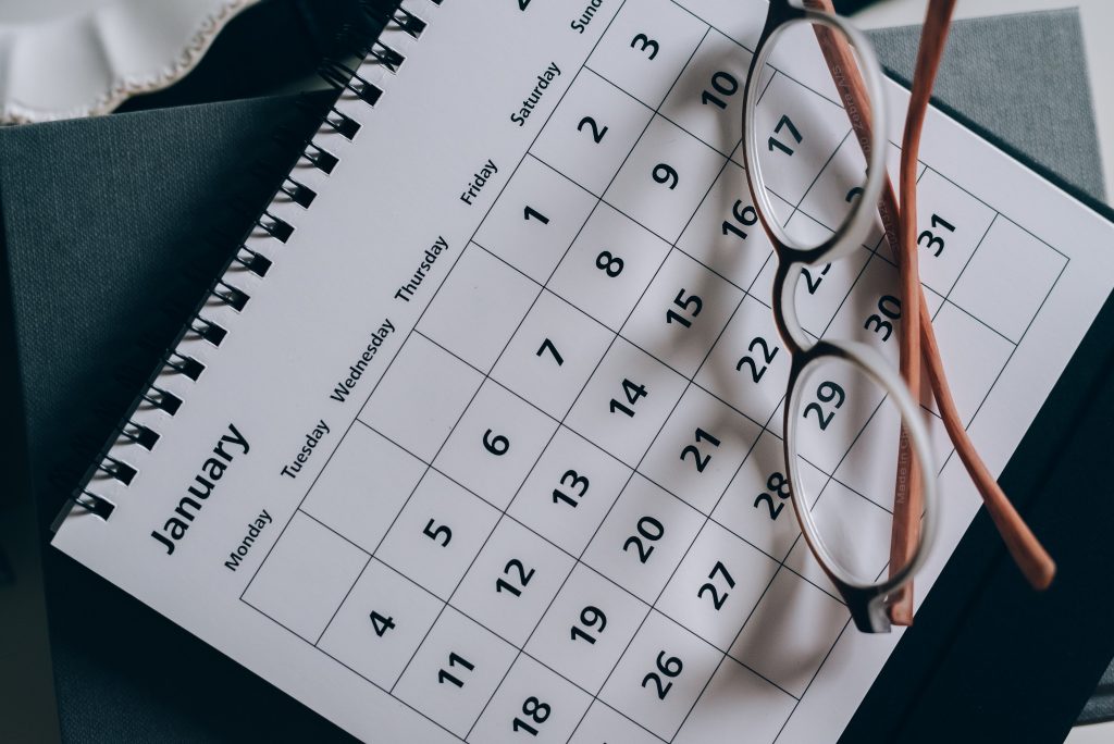 A table calendar lies flat, showing the month of January.  A pair of glasses lies on top