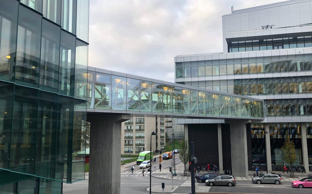 An enclosed glass bridge connecting buildings on two sides of the road below.