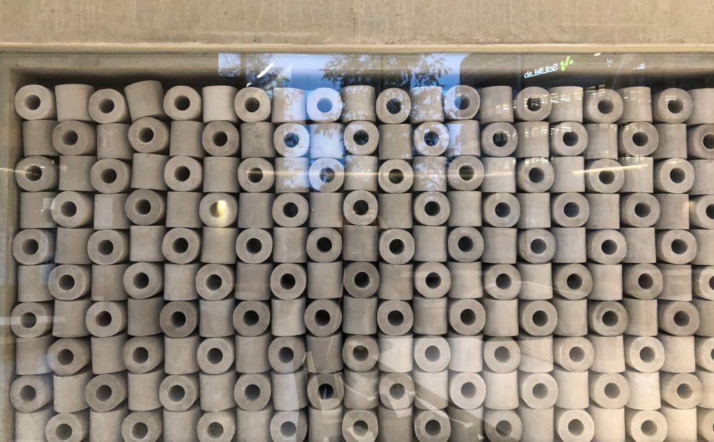 A collection of what looks like toilet paper rolls in a glass wall. A small "SciLifeLab" sign is reflected in the glass.