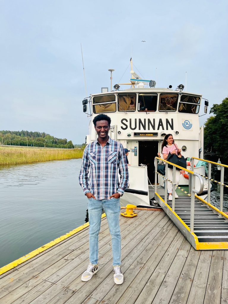 Photo by John of me standing outside the SUNNAN boat, with the boat and water in the background, during our Stockholm Waters adventure.