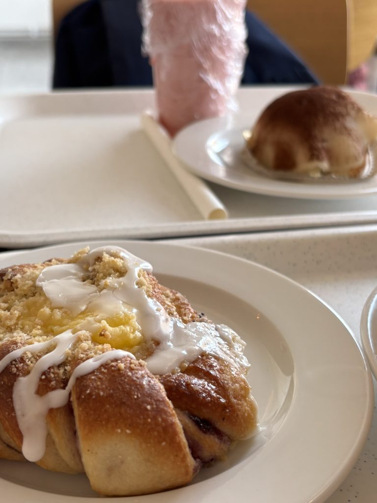 A plate of blueberry bun across from another tray with a strawberry smoothie and another dessert