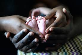 A baby's feet held within the palms of their parents' hands - with the soles showing and a ring on each foot.