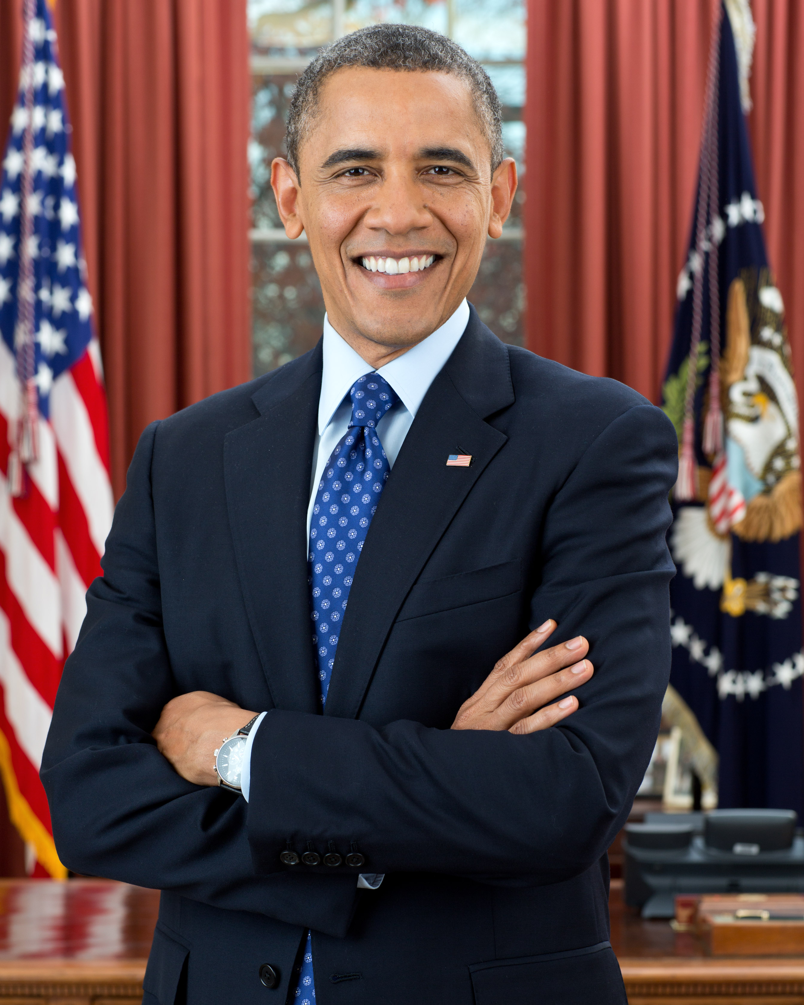 President Obama standing tall with his arms crossed and smiling in the Oval office of the White House.