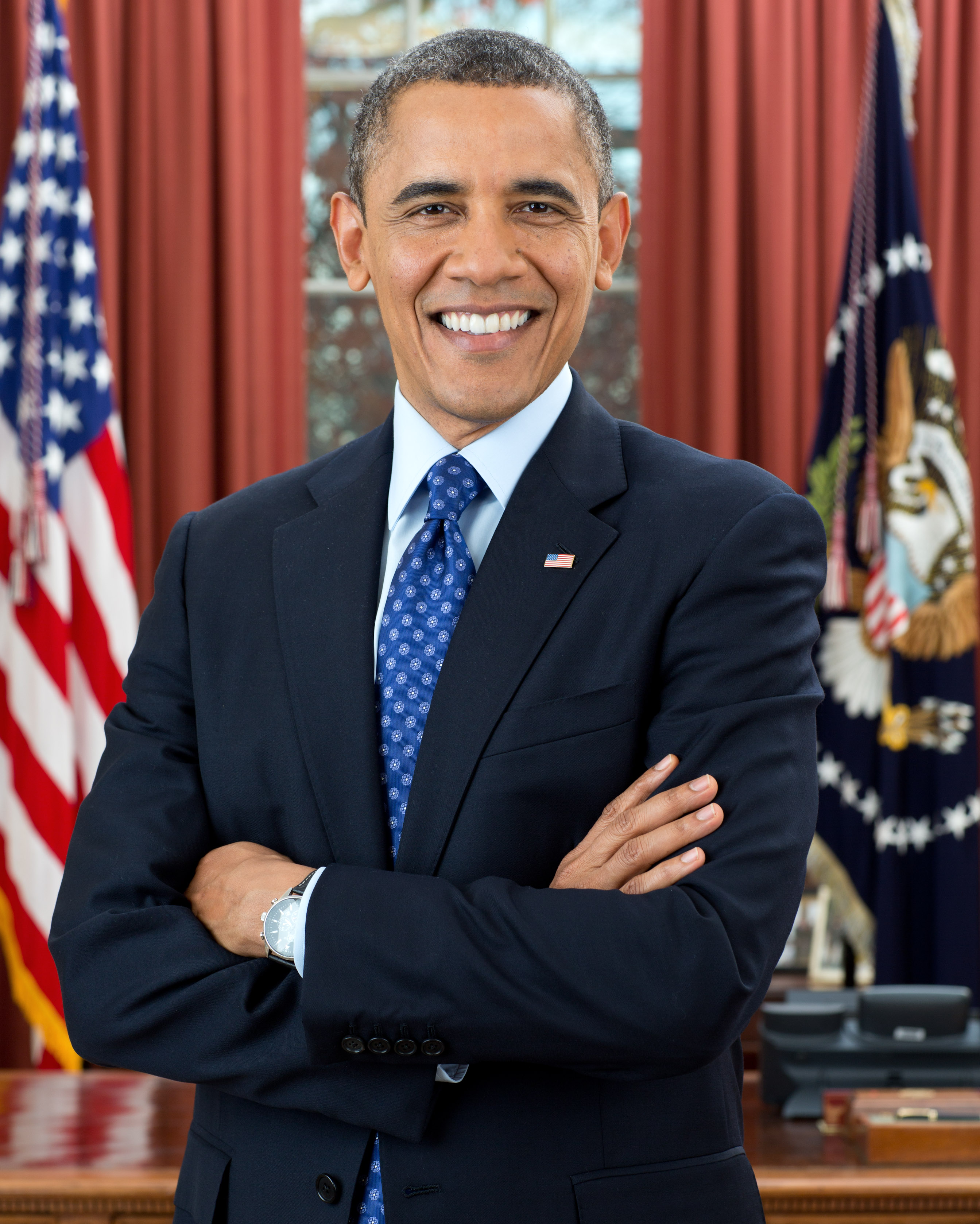 President Obama standing tall with his arms crossed and smiling in the Oval office of the White House.