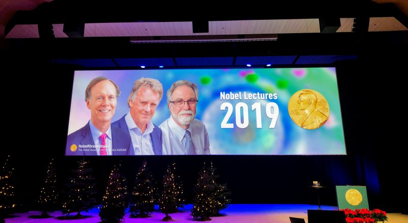 An image showing the the stage and powerpoint slide, the latter with the 3 nobel laureates.