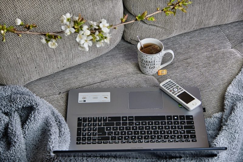 A cozy scene, with a laptop and a mug of coffee on a grey sofa.