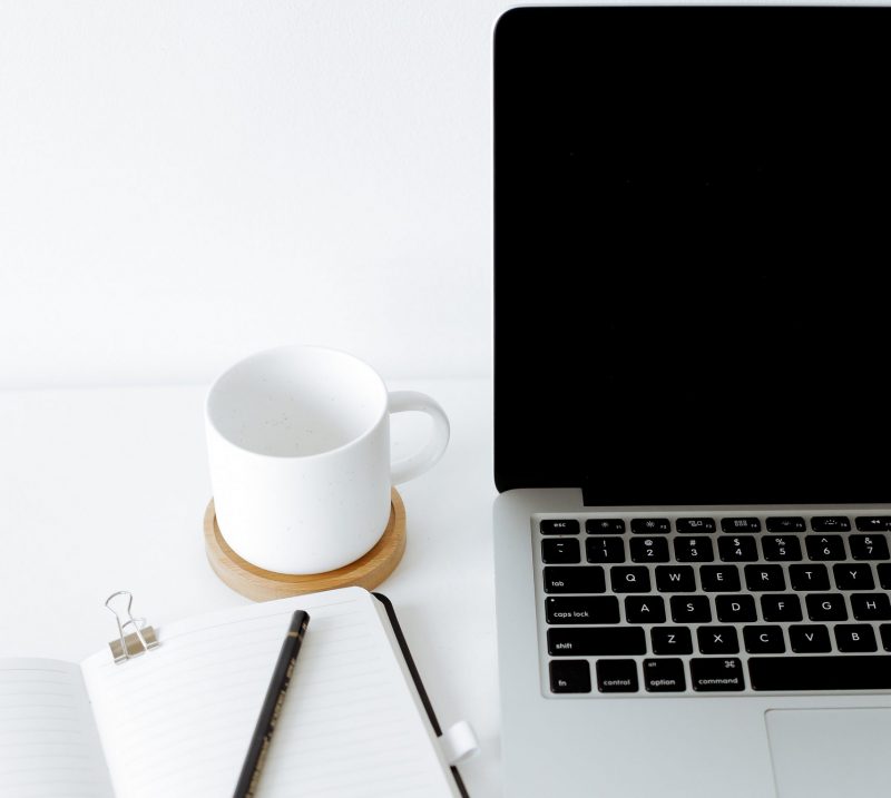 Half of a computer, with a notebook and a cup of coffe