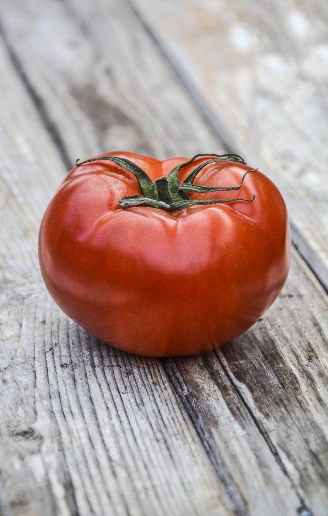 A dark red tomato on a grey wooden surface.