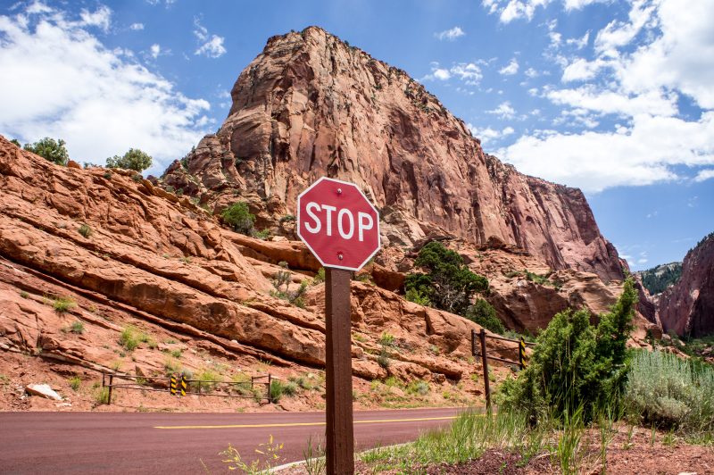 A stop sign with a rocky mountain as the backdrop and a blue sky