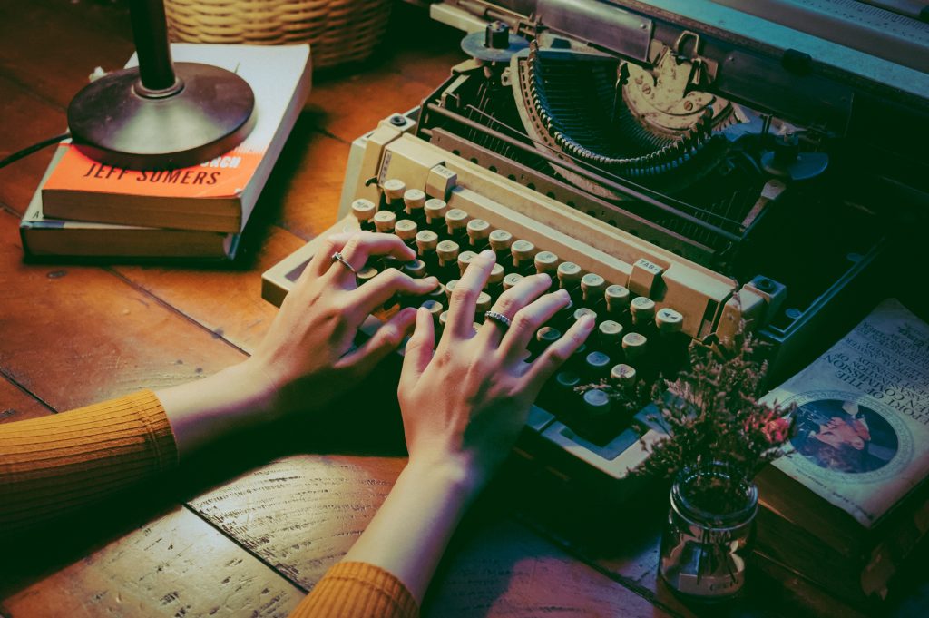 Two hands on a typewriter in a dimly lit and rustic setting