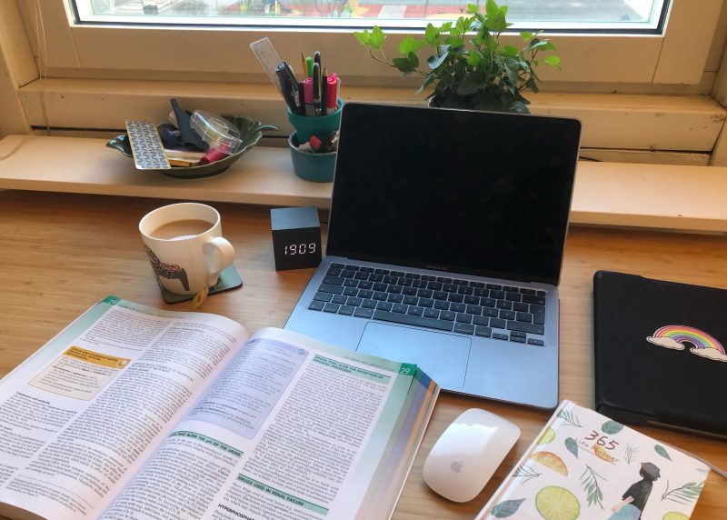 A desk with a laptop, tea, a planner, and an open book