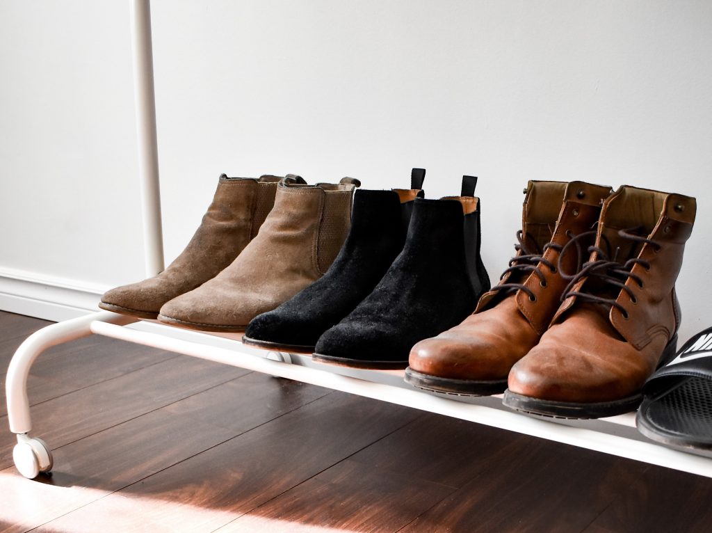 3 pairs of boots on a shelf, two suede boots that are brown and black, and one pair of leather boots. 