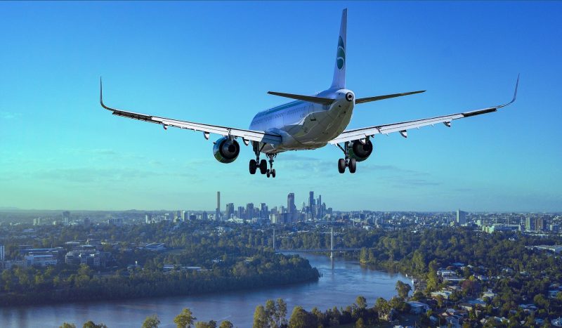 An airplane flying towards a big city in a bright blue sky