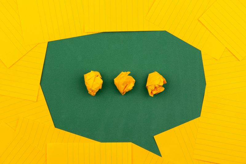 a green speech bubble with elipses made of crumpled yellow paper, framed by yellow paper
