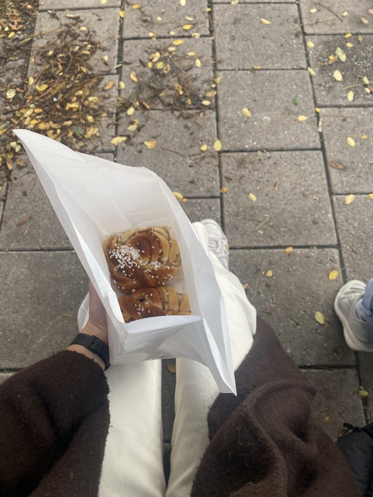 A photo of a white paper bag containing two kanelbullar, held on someone's lap.