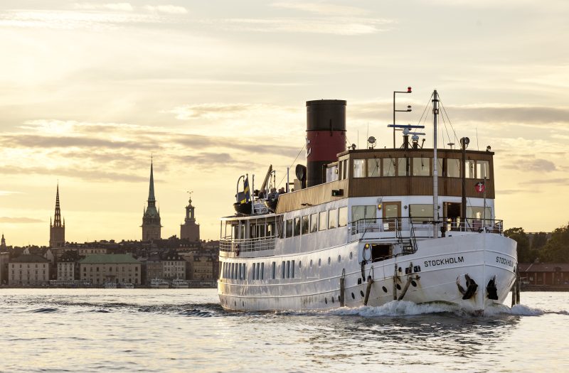 Photograph by Jeppe Wikström capturing a boat on Stockholm's waters with the city's iconic buildings in the background, part of the SUNNAN Stockholm Discovery.