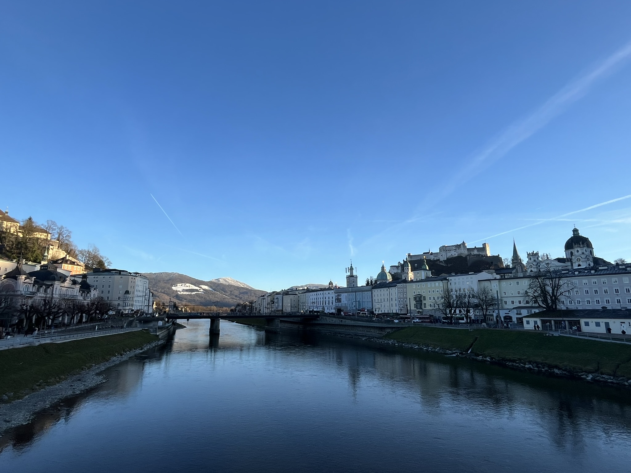 A scenic picture of a river running through the center with Salzburg city on both sides on a sunny day.