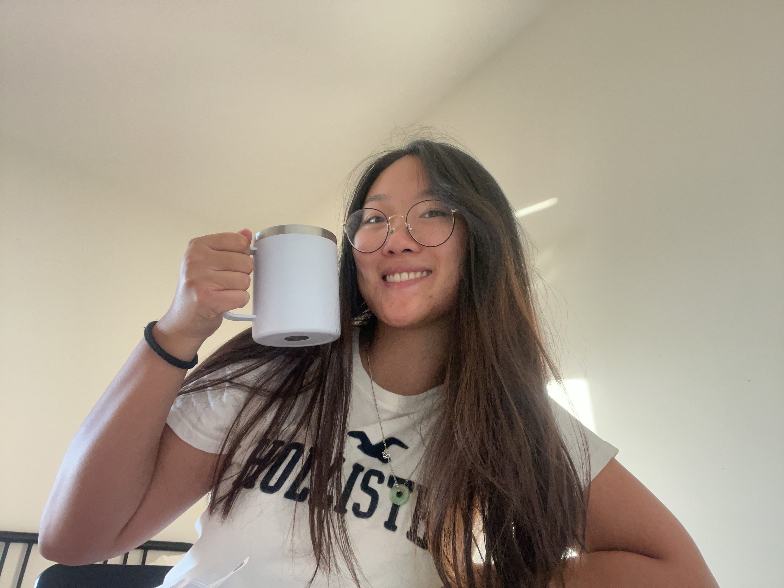 A girl holding a cup and smiling in a room.