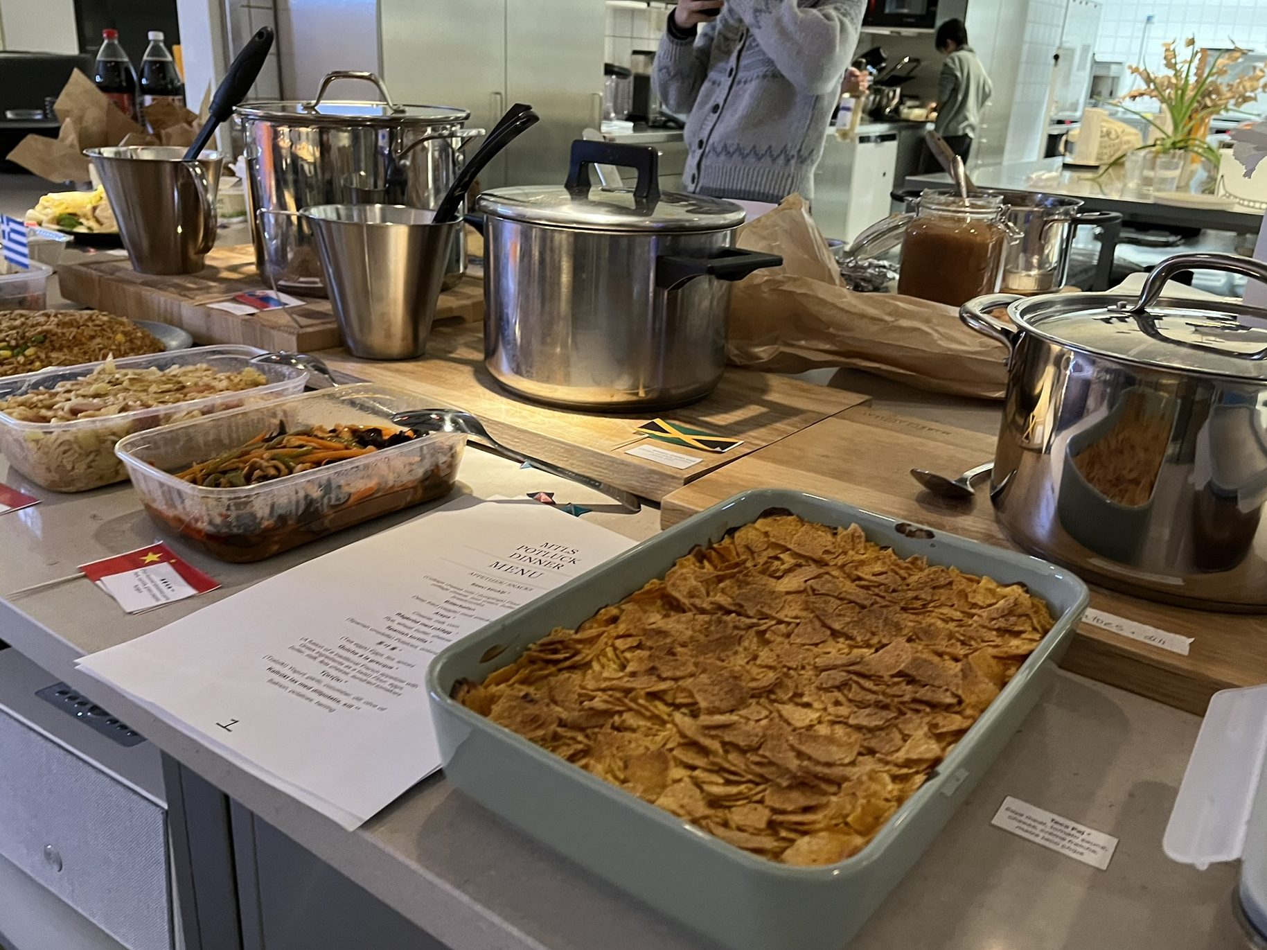 A spread of dishes with their names and country flags for the cultural potluck.