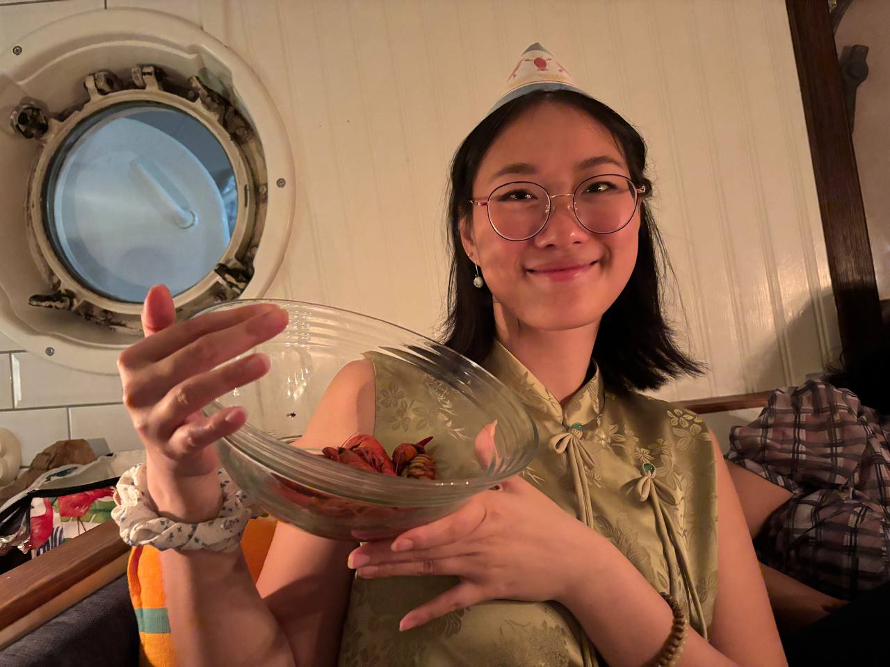A girl holding a bowl of crayfish wearing a crayfish themed party hat.