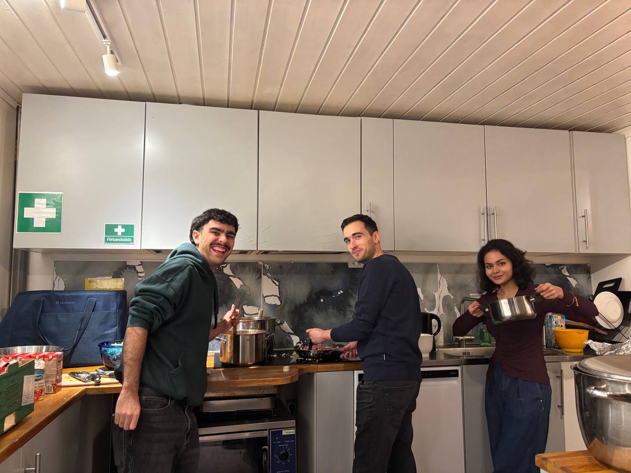 Three people posing in the kitchen with pots and ingredients.