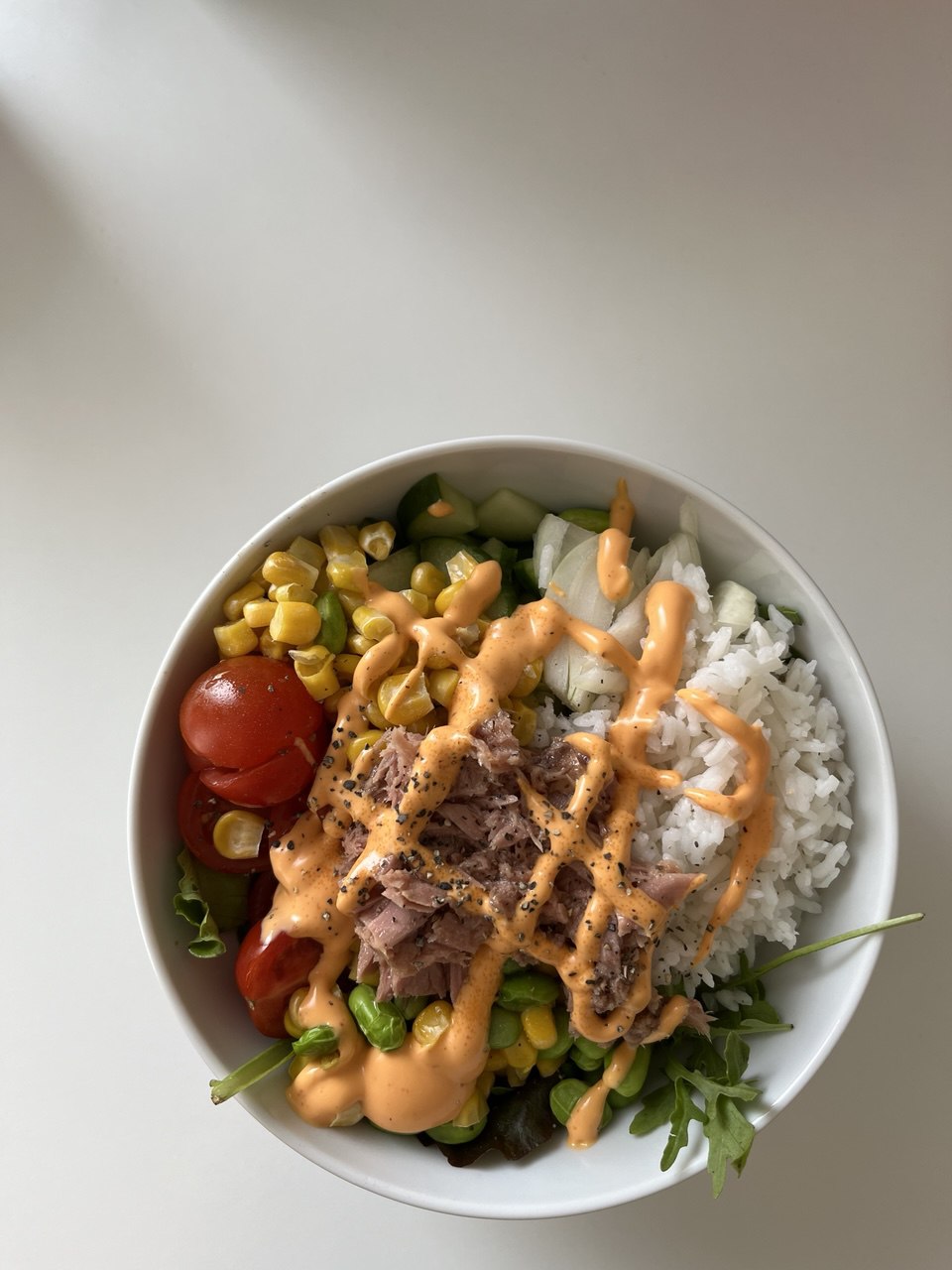 A poke bowl made with tuna, rice, corn, salad greens, tomato, and chilli mayo.