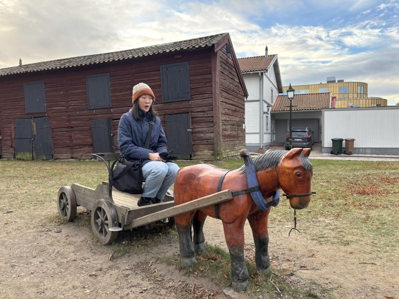 A girl looking shocked on the carriage of a miniature horse statue/display