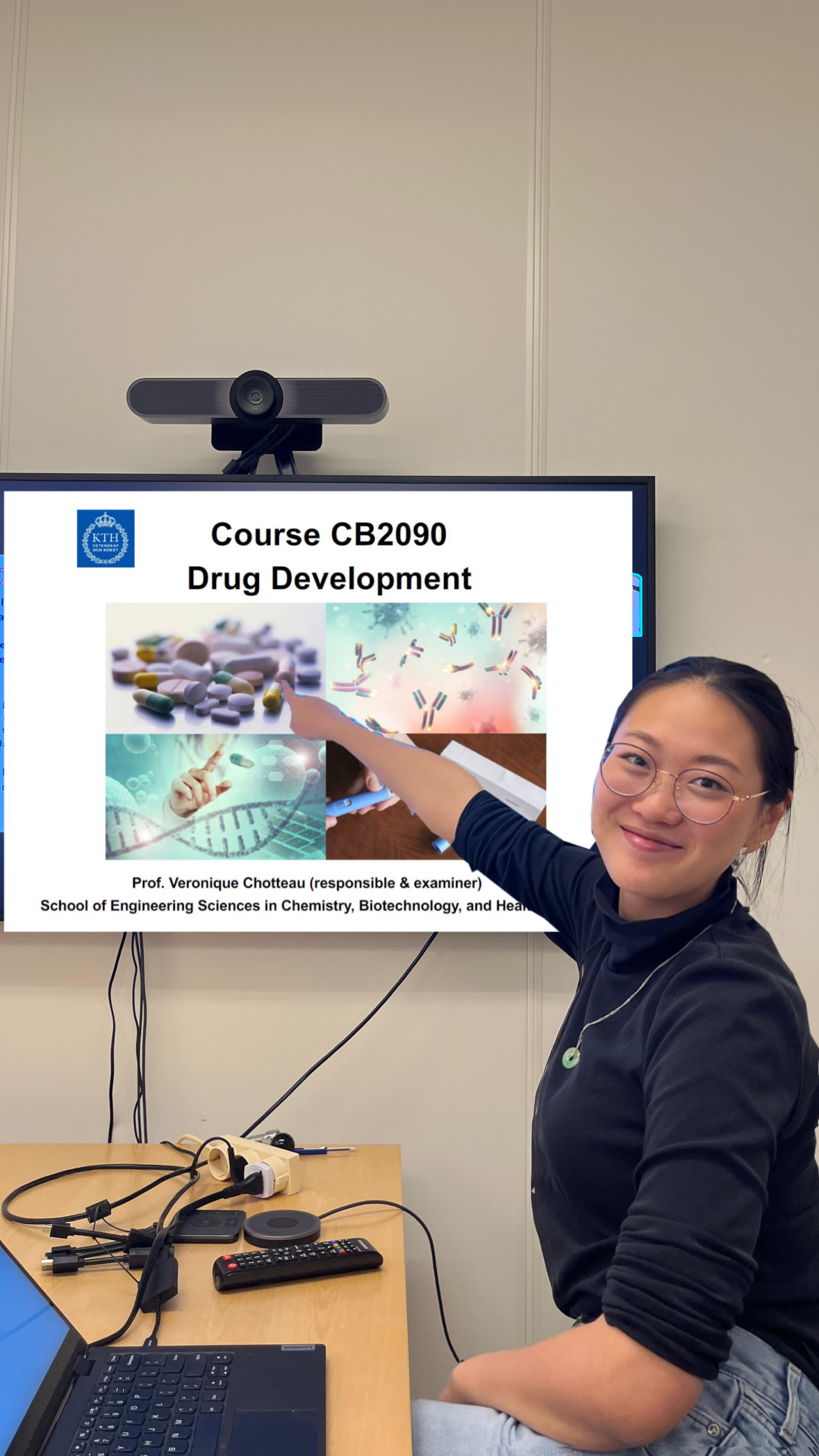 A girl pointing to a TV screen that shows an edited slide of the Drug Development course. The edited slide onto the TV is covering a zoom screen.