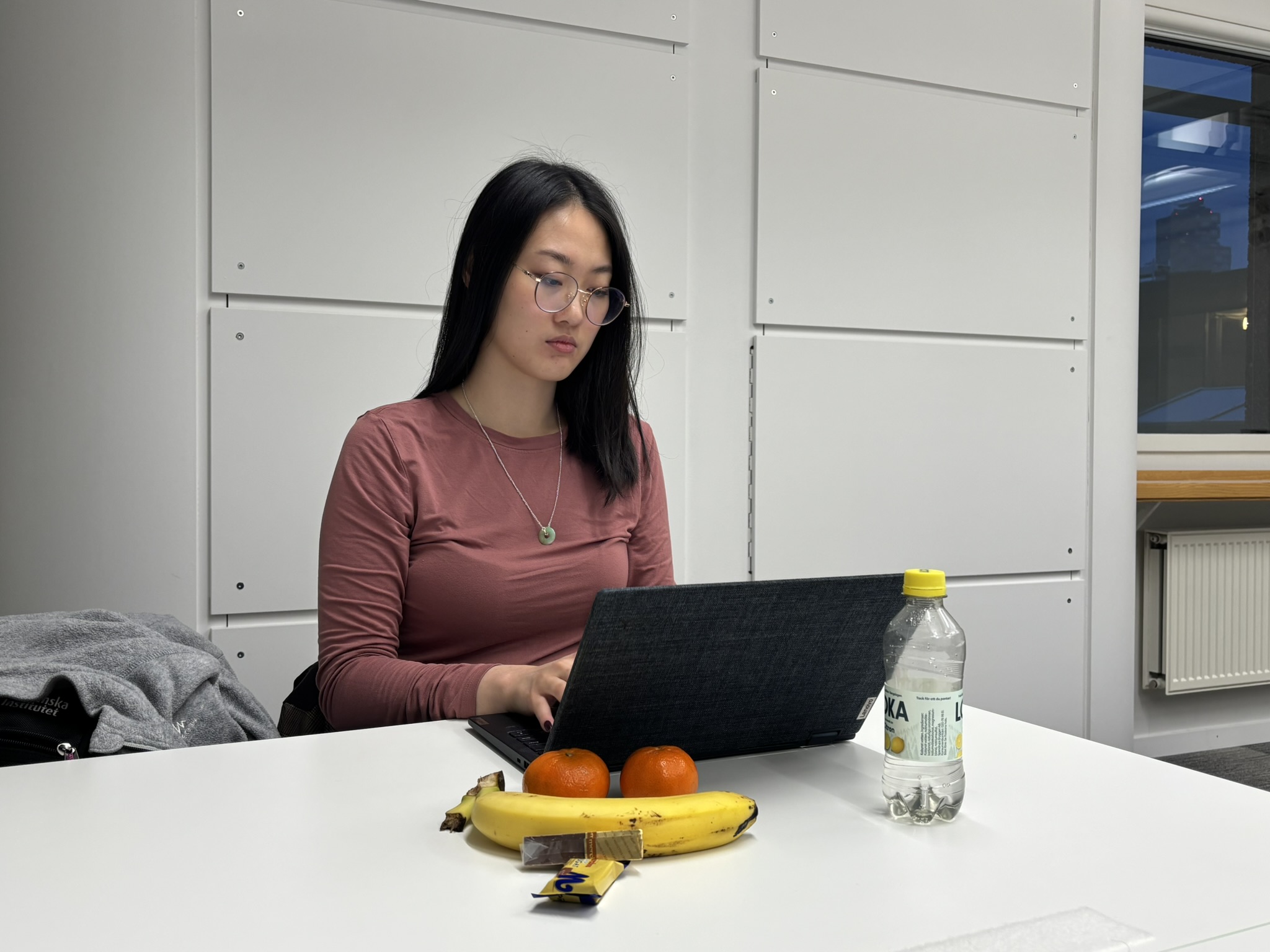A girl staring intensely at her laptop with some fruits and snacks laid out in front of her.