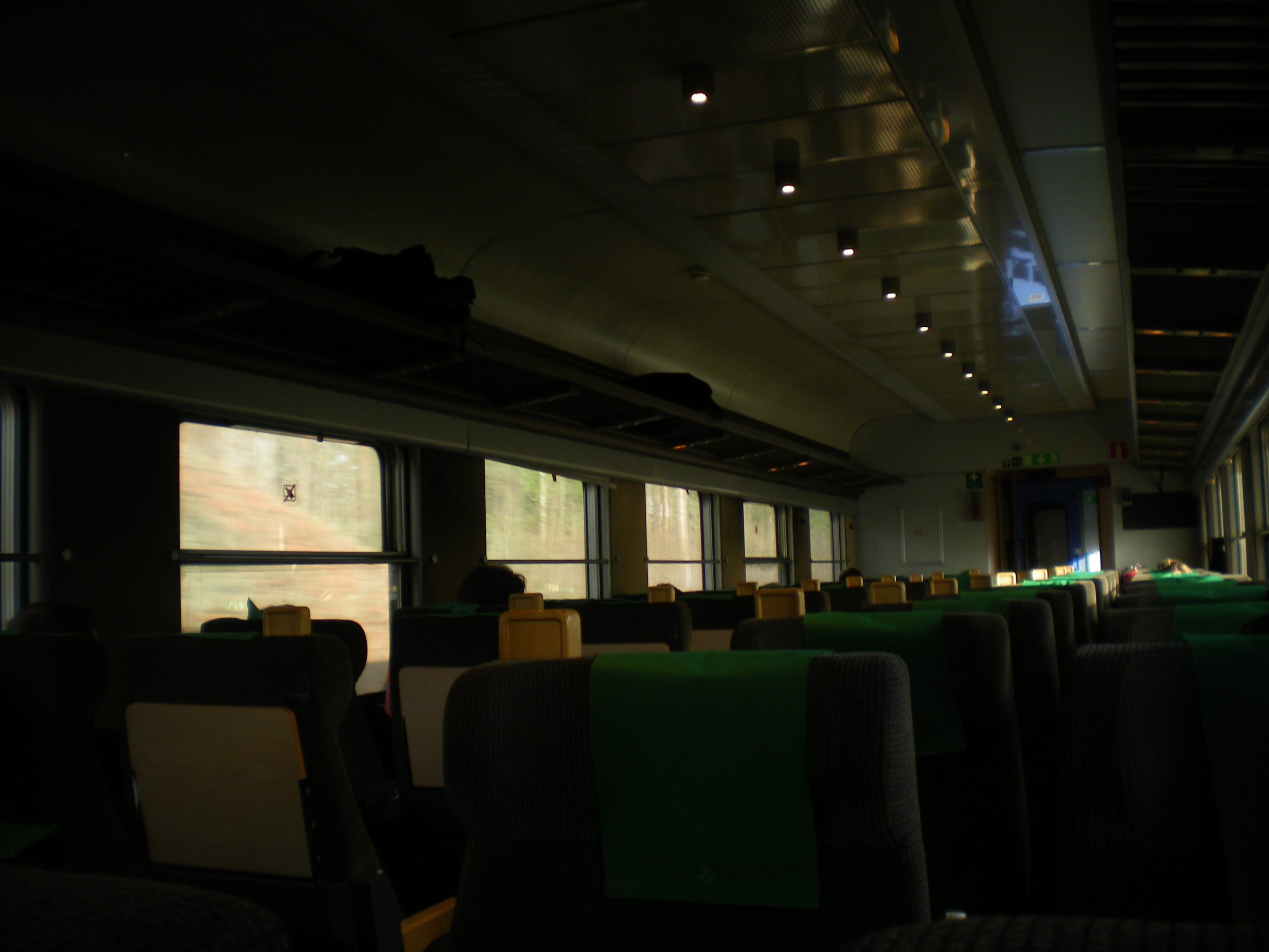 Inside of an old train with the sun coming in through the windows. The seats are all emoty with two on each side of the aisle. 