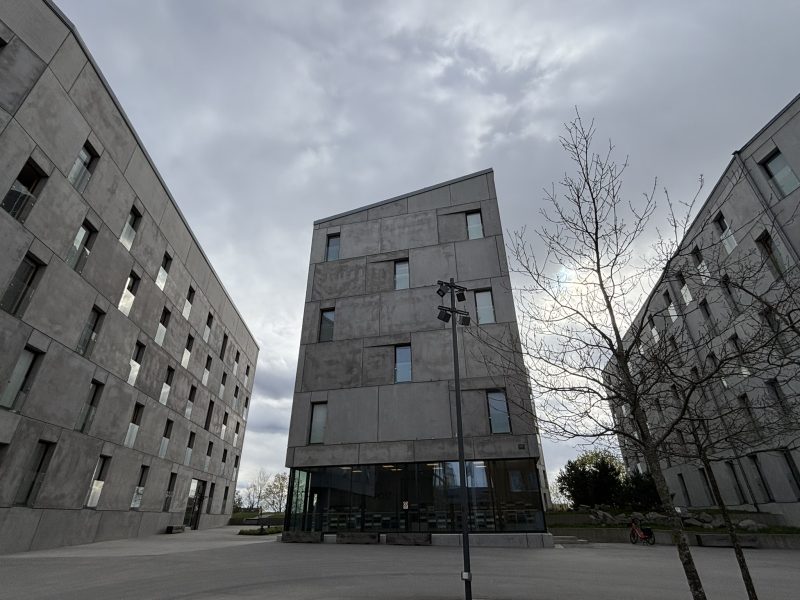A set of three student housing buildings against a cloudy sky. They are all grey with a brutalist design