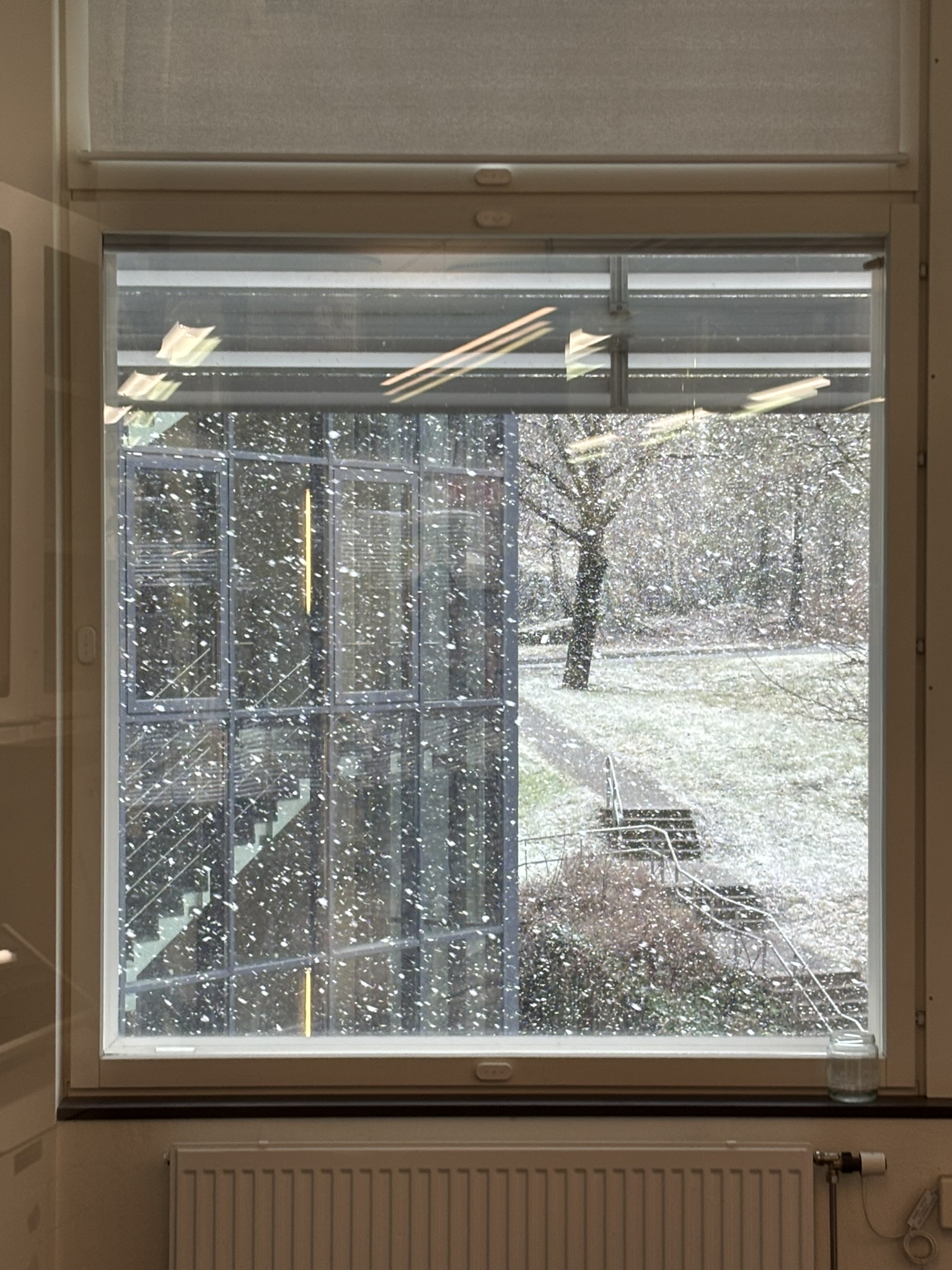 A window view showing snow blowing around with the other side of a building as part of the view and a staircase to the right. 