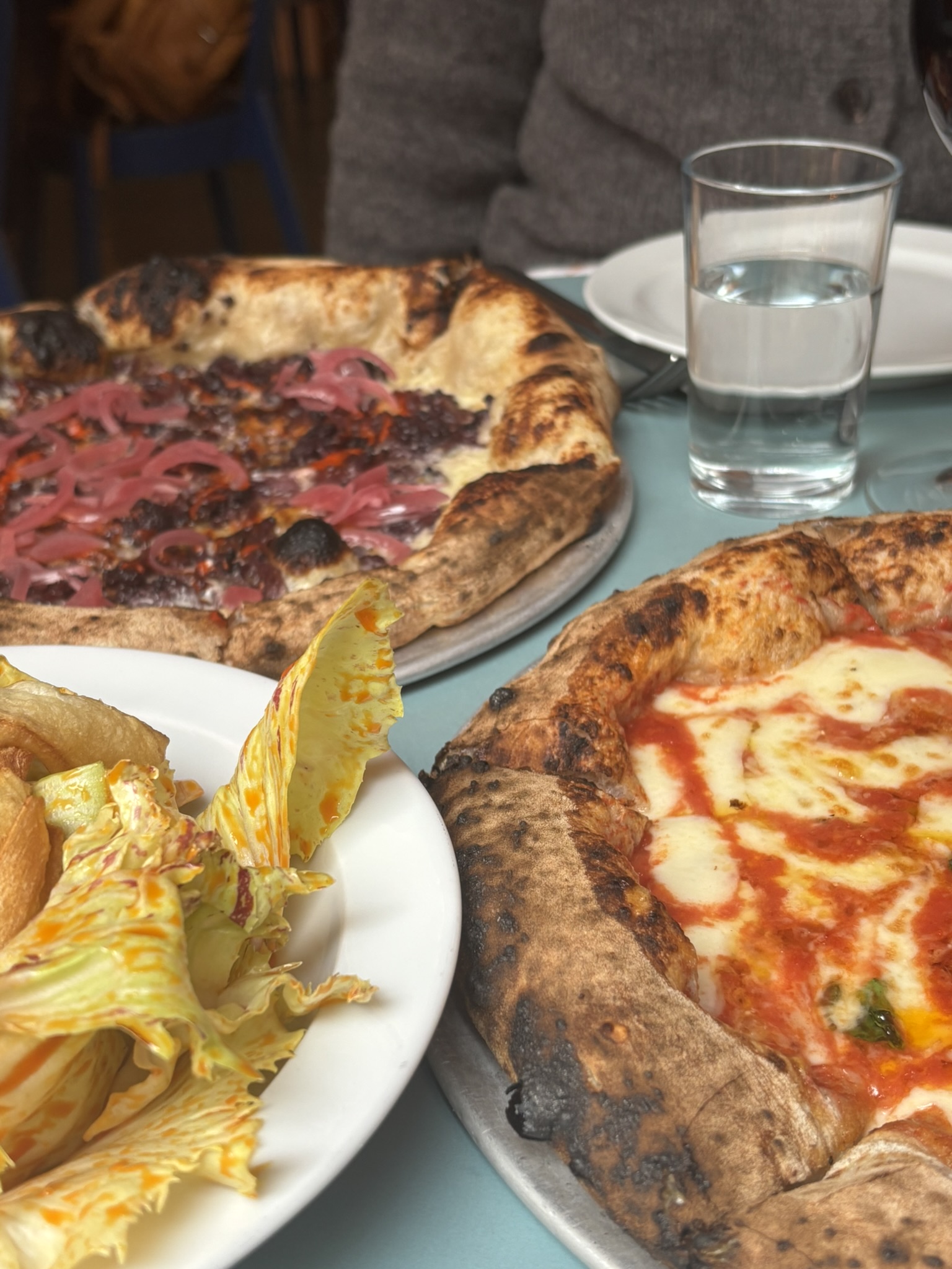 A table with three dishes. Two of which are personal pizzas and one is a salad with an orange coloured Vinaigrette. 