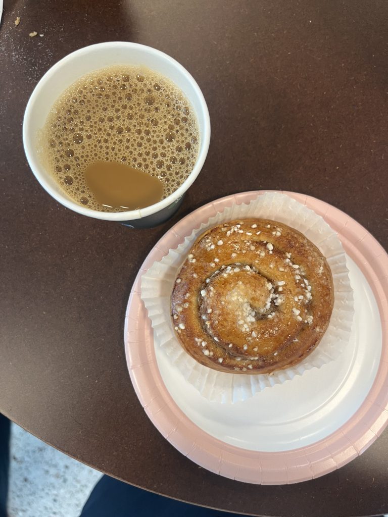 A cup of coffee and a kanelbulle on a plate on a table.